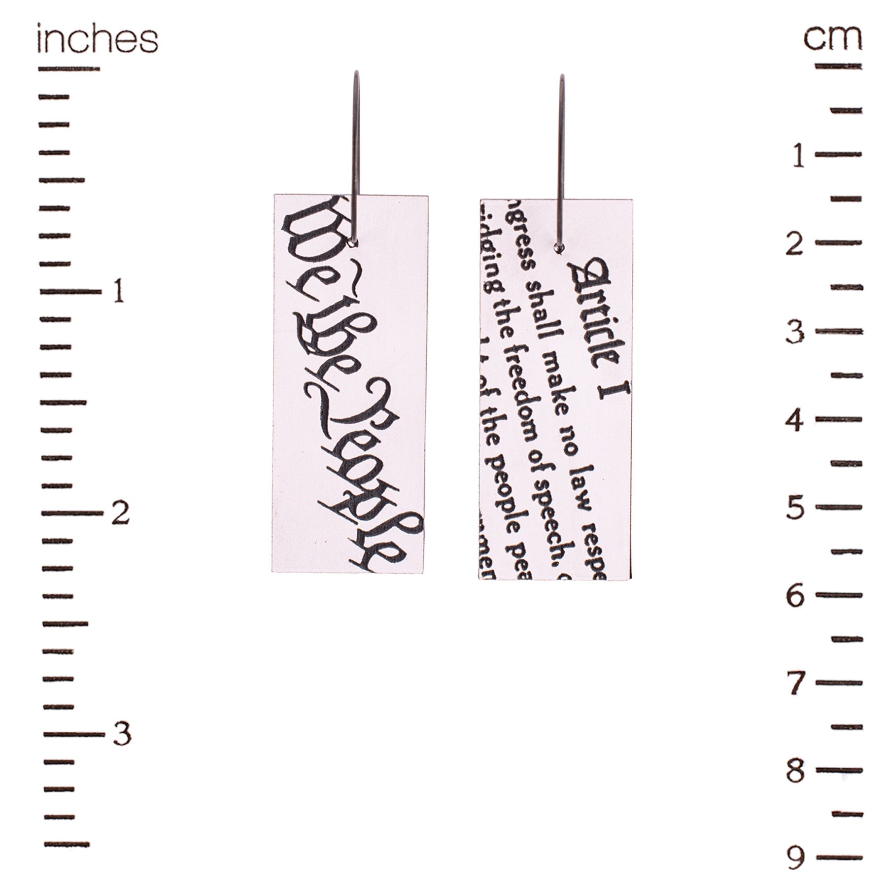 Earrings with text from the Constitution measured against a ruler.