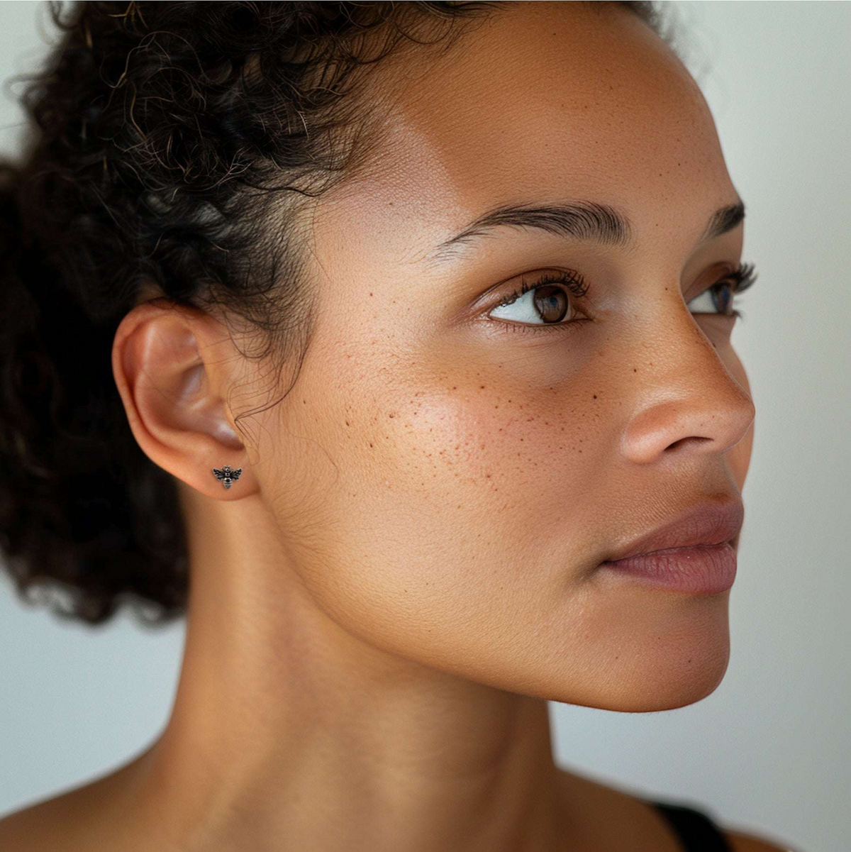 Tiny recycled sterling silver bee stud earrings with intricate wing detail, worn on an ear.