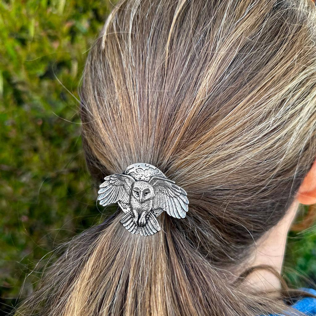 Silver metal ponytail holder with a detailed owl design, featuring outstretched wings and a moon backdrop. Handcrafted hair accessory.