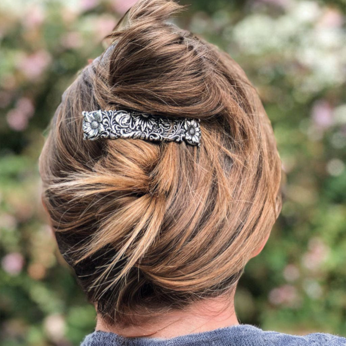 Silver barrette with intricate wildflower engraving, 70mm size, holding back blonde hair in a bun.
