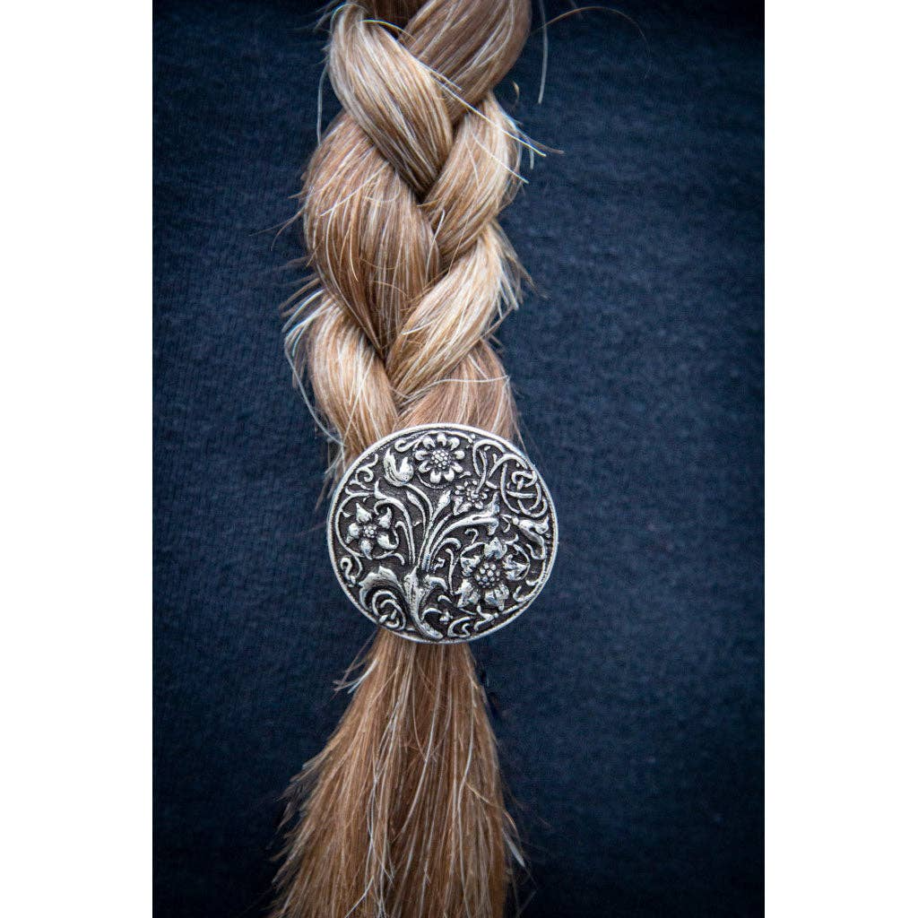 Circular silver ponytail holder with intricate wildflower design, attached to a blonde braid.